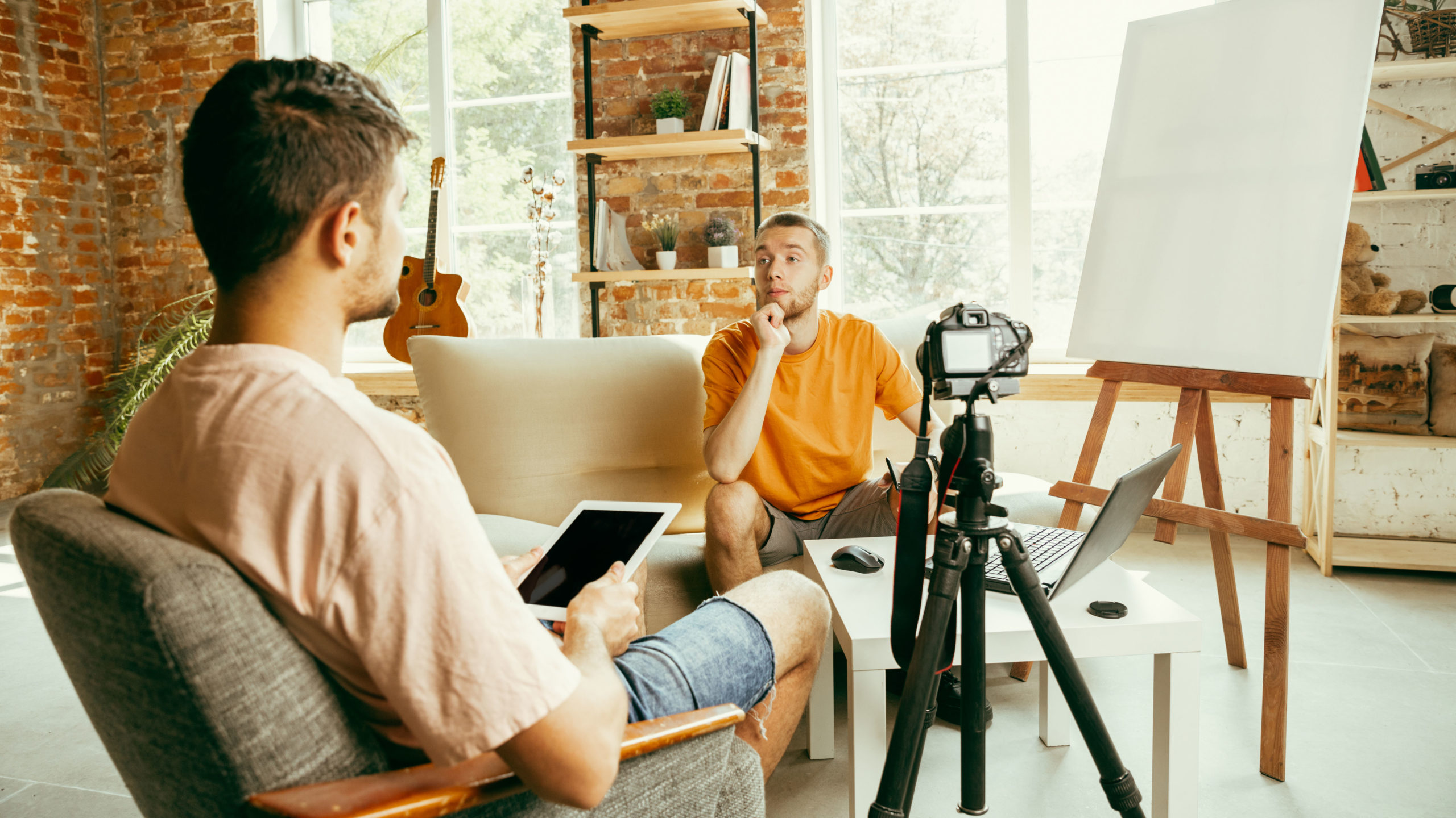 Two young male bloggers with professional camera recording video interview at home